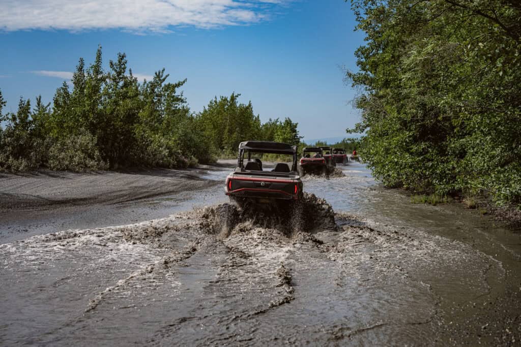 utv splashing through a muddy creek on a bluebird day in the Alaskan wilderness