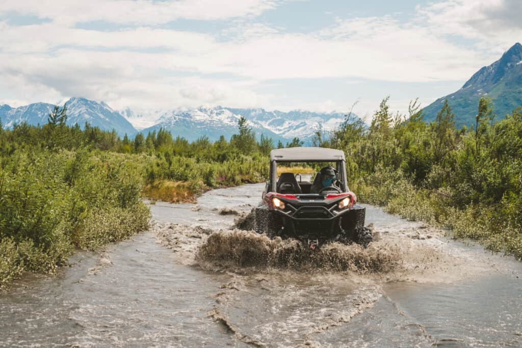 utv driving through a creek near Anchorage Alaska with mountains in the background